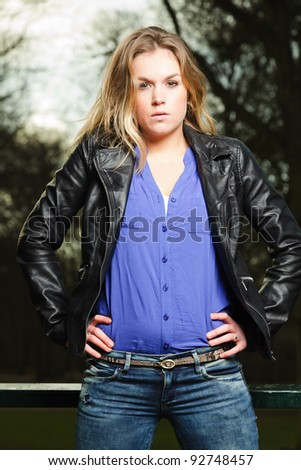 Pretty young woman with long blond hair wearing blue shirt and black leather jacket outdoors in winter forest
