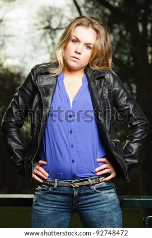 Pretty young woman with long blond hair wearing blue shirt and black leather jacket outdoors in winter forest