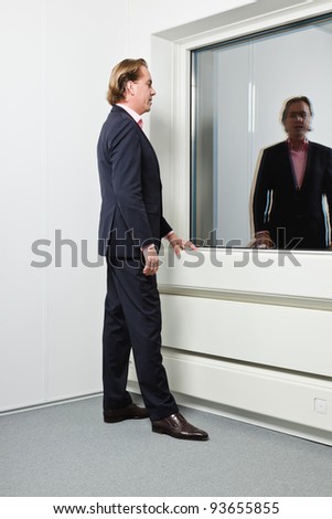Young business man blond hair wearing blue suit and pink shirt in front of window.