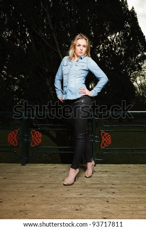 Pretty young woman long blond hair in winter forest. Wearing blue jeans shirt and black pants.