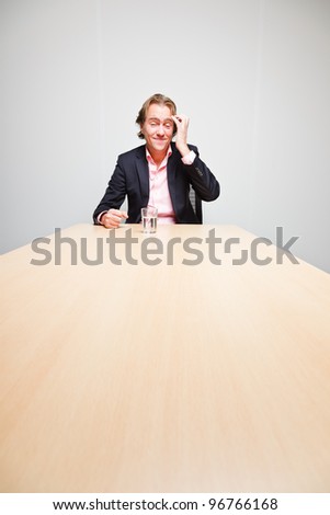 Business man with blond hair sitting bored behind table in boardroom isolated on white background
