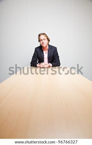 Business man with blond hair sitting bored behind table with glass of water in office isolated on white background