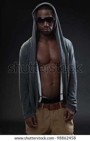 Young black man urban style wearing dark sunglasses looking tough isolated on dark background. Studio portrait.
