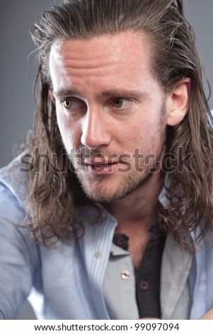 Young man long hair with expressive face wearing blue shirt. Isolated on grey background.