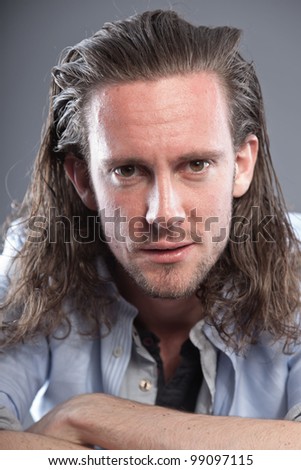 Young man long hair with expressive face wearing blue shirt. Isolated on grey background.