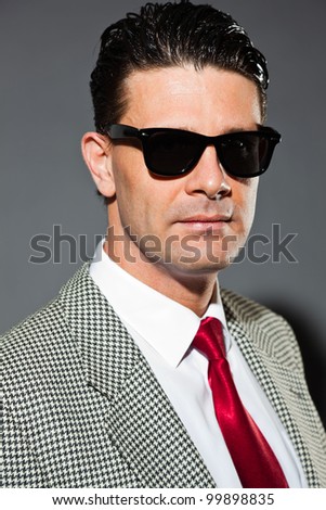 Business man with light grey suit and red tie isolated on dark background. Wearing black sunglasses. Studio shot.
