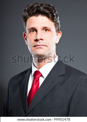 Business man with dark grey suit and red tie isolated on dark background. Studio portrait.