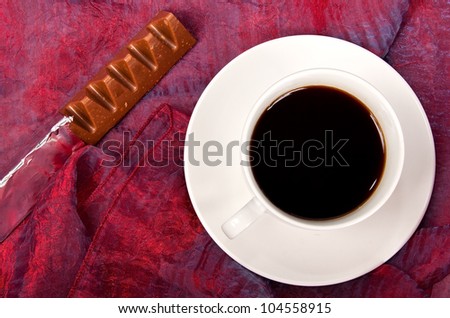 White cup of coffee with chocolate on a red table cloth