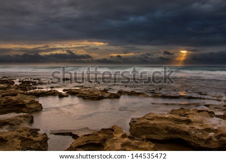 Sunrise landscape of ocean with waves clouds and rocks on beach