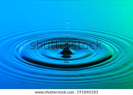 Water drop close up with concentric ripples on colourful blue and green surface