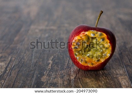 Red apple with bite open passion fruit inside on a wood surface