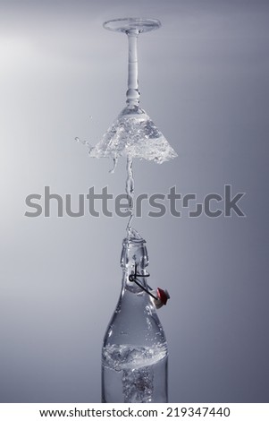 Clear water pour out of bottle splash into a glass with grey back lighting upside down