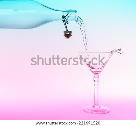 Clear water pour out of bottle splash into glass witha a pink and blue back lighting