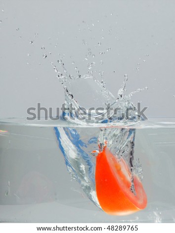 Tomato falling into water bowl, creating a wet splash which is frozen in time for an ideal background