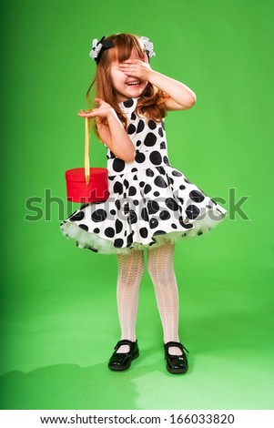 Happy emotional little girl holding christmas red box on a green background. Model in vintage black and white dress with peas print.