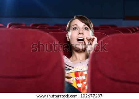 Young surprised woman eating popcorn in the movie theater