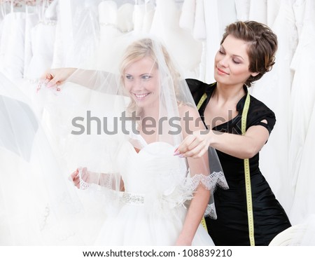 Shop assistant sets the veil of the bride, white background