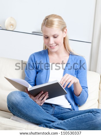 Beautiful woman reads the book lying on the white leather sofa