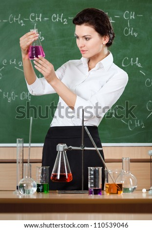 Smiley chemistry teacher examines conical flask with pink liquid