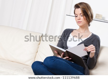 Young girl reads the book sitting on the white leather sofa
