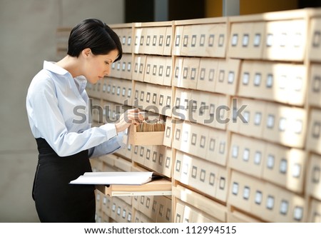 Woman seeks something in card catalog composed of set of wood boxes at the library. Knowledge