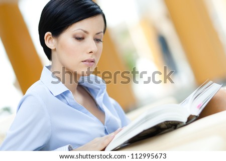 Business woman sits at the sofa reading interesting book at the hall