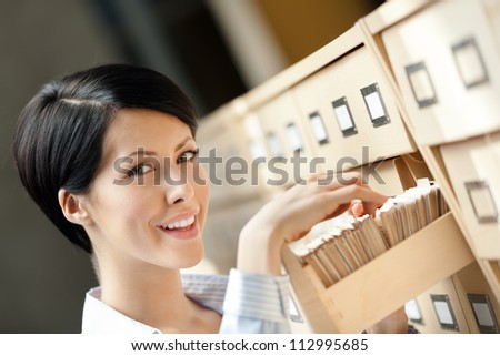 Woman seeks something in card catalog composed of set of wood boxes at the library. Study