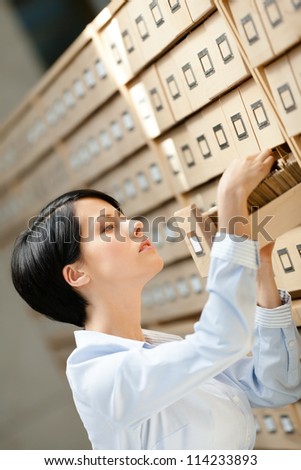 Woman looks for something in card catalog composed of set of wood boxes at the library. Education