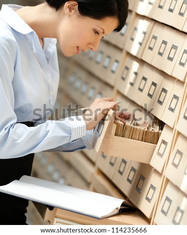 Pretty woman searches something in card catalog composed of set of wood boxes at the library. Education