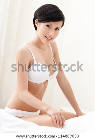 Halfnaked sexy woman sits on the double bed with white bed linen