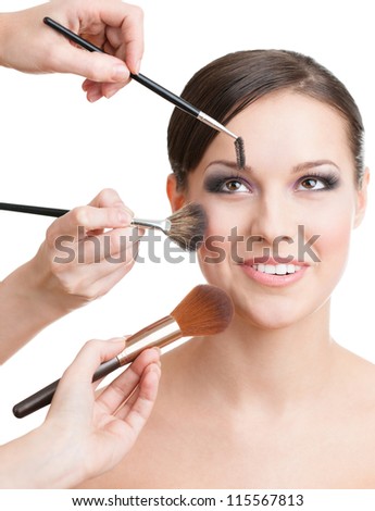 Three hands of makeup artists applying cosmetics on the woman\'s face with brushes, isolated on white