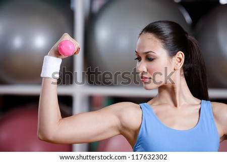 Young woman works out with dumbbells in gym to develop muscles. Strength activity