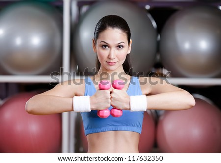 Young woman training her muscular system with dumbbells in gym