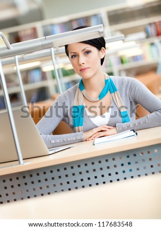 Female student working on the silver laptop sitting at the desk at the library
