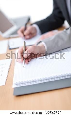 Business people making notes in notebooks sitting at the table. Close up of hands