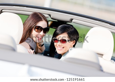 Two happy girls sitting in the car glance back and have fun while having little car trip
