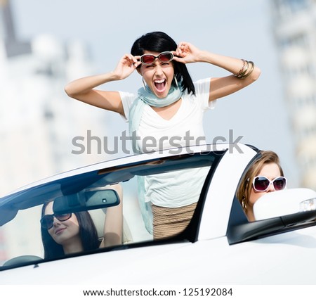 Lovely teenager stands in the car with friends. Girls drive somewhere on vacation
