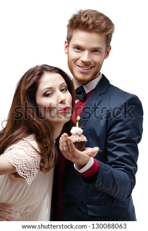 Pretty woman blows out a candle on the birthday cake that her boyfriend presented, isolated on white