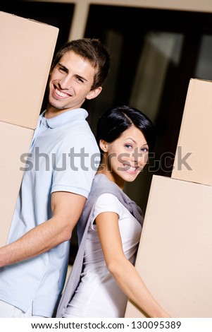Happy couple stands back to back while carrying cardboard packages and moving to new house