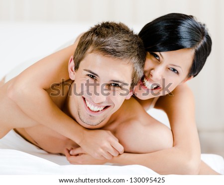 Close up of laughing couple who plays in bed. Woman lying on the back of the man  embraces him