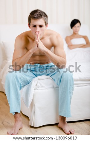Young married couple quarrels in bed-room. Depressed man sitting on the edge of the bed. Focus on man