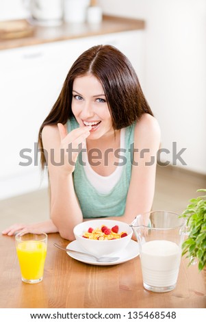 Portrait of the girl eating healthy cereals with milk and strawberry and orange juice sitting at the kitchen table