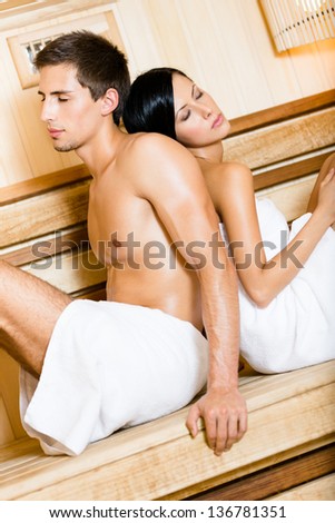 Half-naked man and lady with eyes closed sitting back to back in relaxing sauna