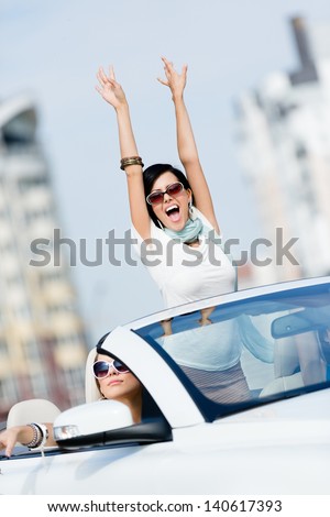 Lovely teenager with her hands up in the car with friends. Girls drive somewhere on vacation