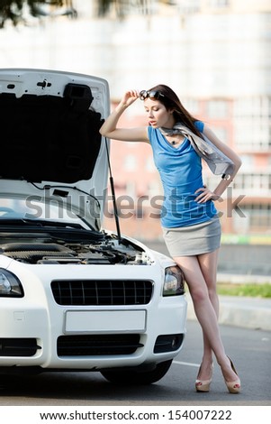 Woman repairing the broken car on the road. Girl stands near opened bonnet of the car after an accident