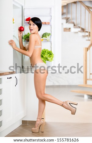 Full length of woman near the opened refrigerator full of vegetables and fruit. Concept of healthy and dieting food