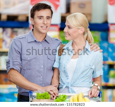 Half-length portrait of couple in the shopping mall with cart full of food. Concept of consumerism and healthy food