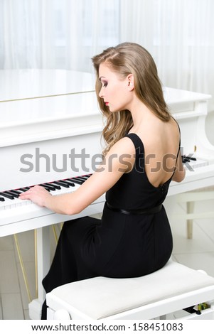 Back view of woman in black dress sitting and playing piano. Concept of music and creative hobby