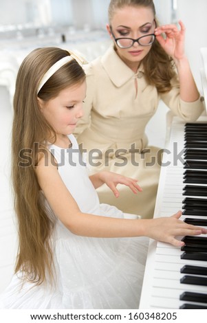 Tutor teaches little girl to play piano. Concept of music study and art
