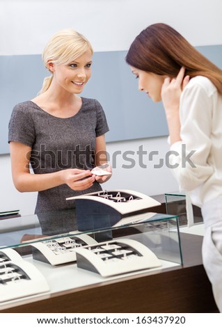 Shop assistant helps lady to choose jewelry at jeweler's shop. Concept of wealth and luxurious life